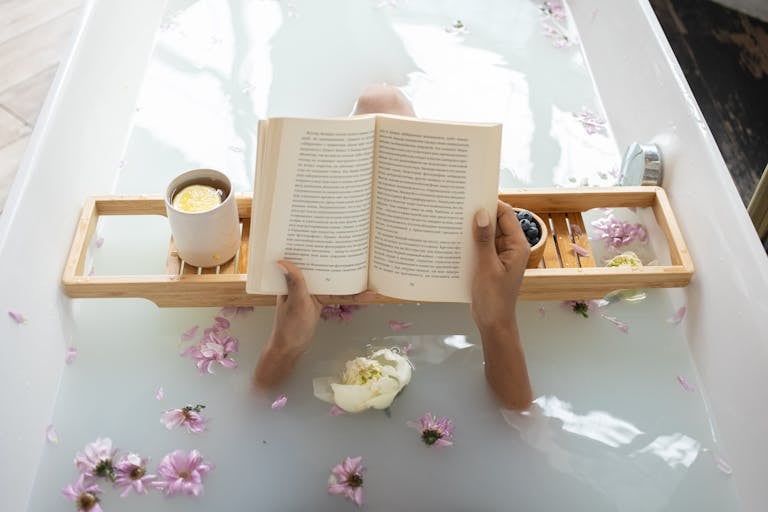 Enjoy a tranquil bath with a book surrounded by flowers and warm tea. Perfect spa day setting.